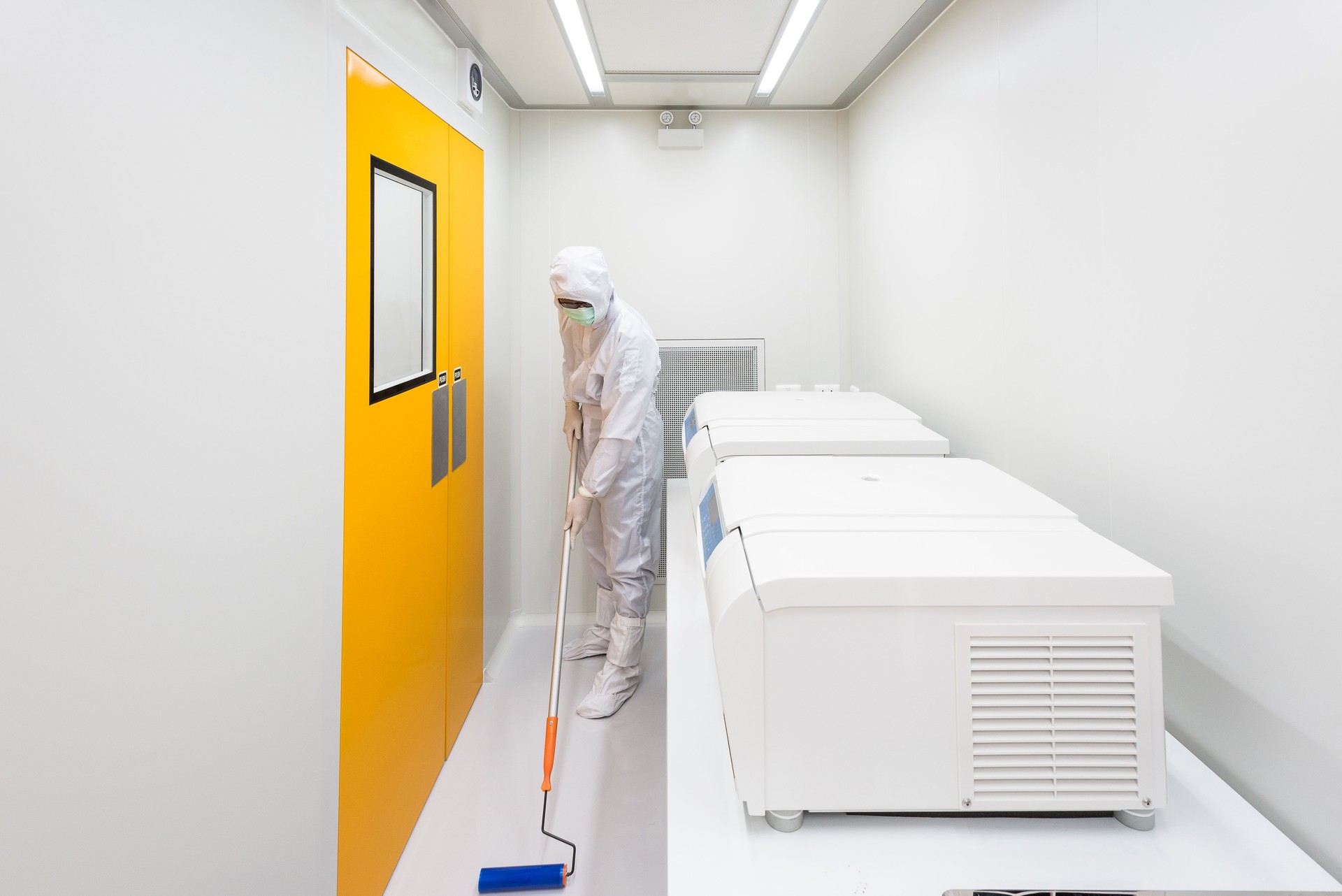 A scientist in sterile coverall gown using lint roller for cleaning laboratory. Cleanroom facility.